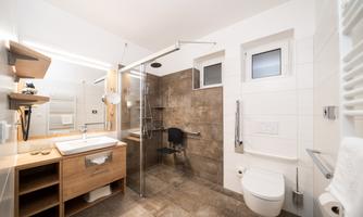 A modern bathroom with a walk-in shower and a wooden vanity. The walls are in neutral tones, and there are large windows for plenty of light.