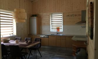 A modern kitchen with wood paneling and large windows. The table is set for six people and the furnishings appear functional and inviting.