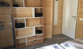 A cozy room with wood paneling and a modern shelf. In the background, a white door and a mirror can be seen.