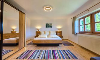 A modern bedroom with a double bed and large windows. The room is bright and cozy, with a colorful rug and modern furniture.
