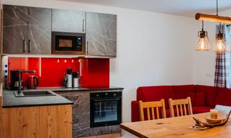 A modern kitchen with wood and stone elements. There is a dining table and a cozy seating area with a red sofa.