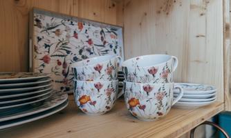 A shelf with decorated cups and plates. The cups display a floral pattern in soft colors.