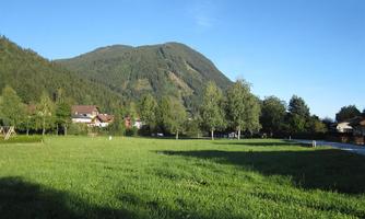 A picturesque landscape with gentle hills and green meadows. In the background, trees and a quiet village can be seen.