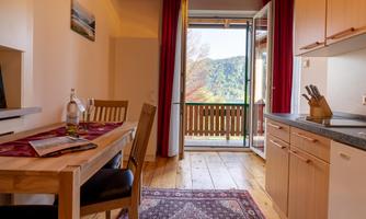 A cozy kitchenette with a dining area and access to a balcony. The windows provide a view of the surrounding nature.