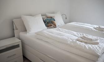 A bright bedroom with two single beds and white bedding. Next to the beds is a nightstand with a reading lamp.