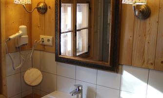 A cozy bathroom with wooden paneling and warm light. On the sink sits a soap dish, and the mirror reflects the warm atmosphere.