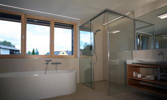 A modern bathroom with a freestanding bathtub and a glass shower. Large windows provide a view of the outdoors and allow plenty of natural light.
