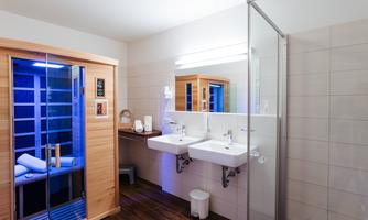 A modern bathroom with a sauna and two sinks. The walls are bright and the floor is tiled.