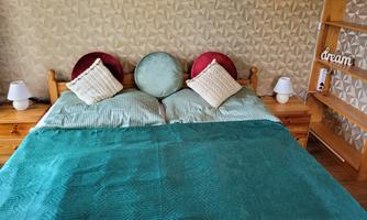 A cozy bedroom with a large bed and red and green pillows. On the bedside table, there are two lamps and a decorative word "dream".