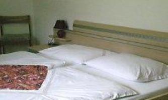 A simple bedroom with a double bed and white bedcovers. Next to the bed is a chair and a lamp.