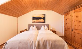 A cozy bedroom with a double bed and wooden ceiling. The decor is simple, with a wardrobe and a picture on the wall.
