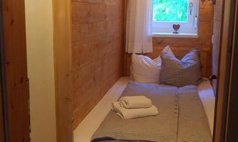 A cozy bedroom with wooden paneling and a window that overlooks green land. The bed is furnished with pillows and fresh towels.