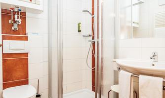 A modern bathroom with a shower, a sink, and a toilet. The walls are tiled in light colors and the furnishings are functional.
