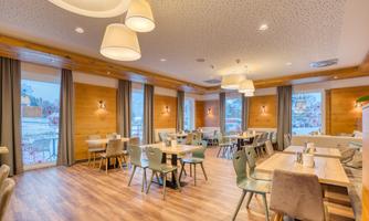 A cozy restaurant with wooden decor and modern furniture. The large windows offer a beautiful view outside.
