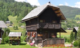 A traditional wooden house in a green landscape. Surrounded by mountains and colorful flowers.