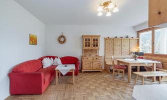 A cozy living space with a red sofa and a wooden table. The walls are light and there are a few decorative elements.