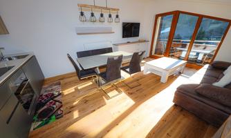 A modern kitchen with a dining area and a cozy living room. Large windows provide plenty of daylight and access to the balcony.
