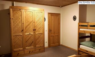 A simple room with a wooden wardrobe and a loft bed. The walls are light, and there is a door on the right side.