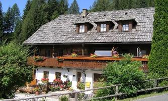 A traditional holiday home with thatched roofing and blooming flowers on the porch. Surrounded by green trees and an idyllic landscape.