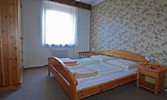 A cozy bedroom with a double bed and a wooden wardrobe. The room has a bright window front and a blooming wallpaper.