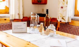 A table in a cozy room, set with glasses, a carafe, and a bottle. Next to the drinks is a welcome note.