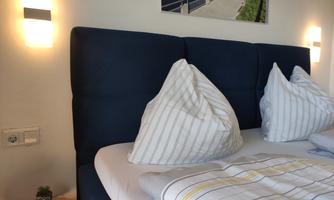 A modern bedroom with a comfortable bed and two large pillows. The walls are bright and there is decorative lighting.
