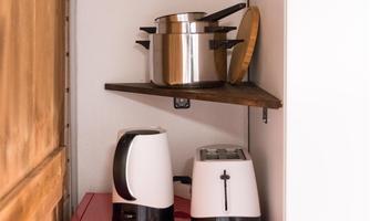A red refrigerator stands in a small nook. Above it, cookware and kitchen appliances are on open shelves.