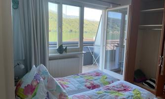 A cozy bedroom with two beds and colorful bed covers. In the background, there are large windows with a view of nature.