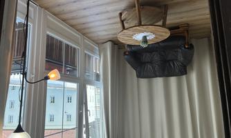 A conservatory with large windows and a cozy black sofa. There is a round wooden table and a floor lamp that creates a warm atmosphere.
