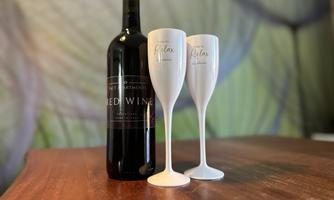 A bottle of red wine stands next to two elegant glasses on a wooden table. In the background, a soft green wall design can be seen.