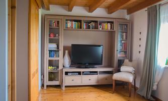 A cozy living space with a bookshelf full of books and a television. The light wooden floor and the windows create an inviting atmosphere.
