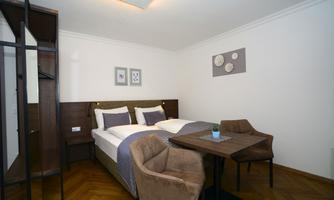 A cozy bedroom with two beds and a small dining table. The decor is modern and inviting, with wooden floors and decorative pictures on the wall.