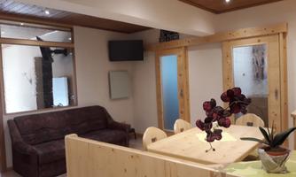 A cozy room with a sofa and a wooden table. There are plants and a TV wall.