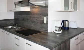 A modern kitchen with a gray countertop and light cabinets. There is a sink, a stove, and various kitchen appliances.