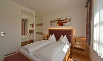 A modern bedroom with two single beds and artistic wall decor. Bright with a large window and a mirror that enlarges the space.