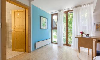 A bright room with blue walls and large windows. The room is furnished with a table and flower decorations.