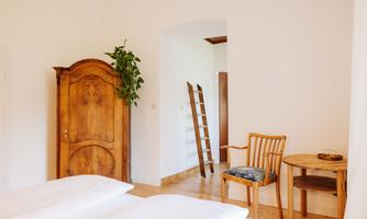 A cozy bedroom with a wooden wardrobe and a ladder. A chair and a small table complement the room, which appears bright and inviting.
