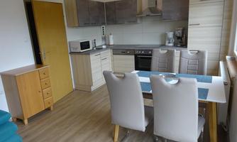 A modern kitchen with a dining table and chairs. The cabinet and appliances are in neutral colors.