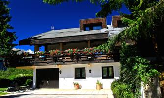 A charming house with a balcony adorned with flowers. Surrounded by trees and clear skies.