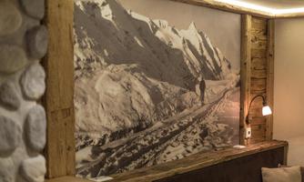 An elegant atmosphere with a large black-and-white mural of snow-covered mountains. In the foreground, rustic wooden elements and a cozy seating area can be seen.
