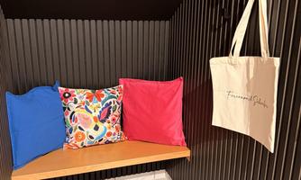 A cozy seating area with colorful pillows in blue, pink, and a vibrant pattern. A fabric bag hangs on the wall beside it.
