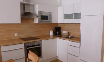 A modern kitchen with white cabinets and wood paneling. It is equipped with a stove, a refrigerator, and a microwave.