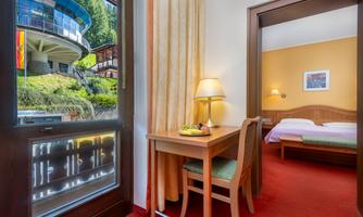 A cozy room with a table and chair. Through the window, there is a view of a green landscape.