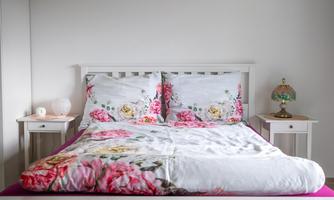 The large bed with the floral bedding looks bright, friendly, and inviting. On the left and right are bedside tables with soft light for cozy reading evenings. Ideal for couples who want to retreat to a soft, quiet nest after an active day by the lake.