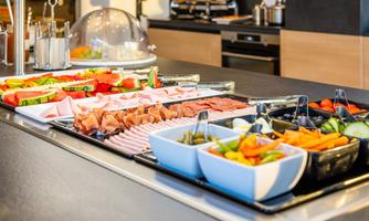 A rich breakfast buffet with fresh fruit, vegetables, and cold cuts. The selection is diverse and attractively presented.