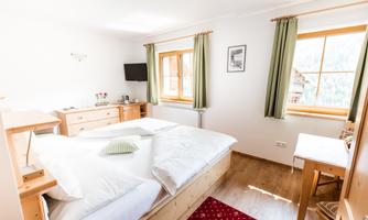 A bright bedroom with a double bed and wooden furniture. The large windows provide ample daylight.