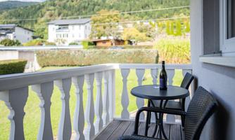 A cozy balcony with a small table and two chairs. On the table stands a bottle, surrounded by a beautiful green landscape.