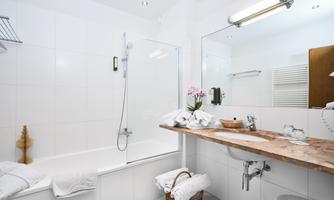 A modern bathroom with a bathtub and a shower. There are fresh towels, toiletries, and a stylish wooden surface at the sink.