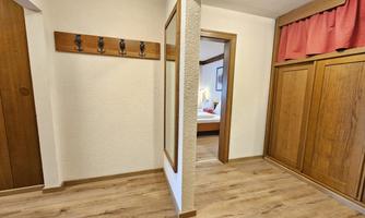 A simple and cozy foyer with wooden paneling. Coat hooks hang on the wall and a large mirror is visible.