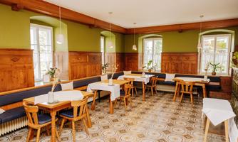 A cozy restaurant with wooden furniture and tables covered with white tablecloths. The walls are painted in a soft green color and large windows let in plenty of light.